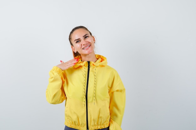 Portrait of young lady with hand over chest in yellow jacket and looking charming front view