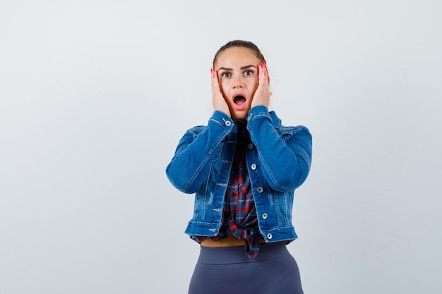 Portrait of young lady with hands on cheeks in shirt, jacket and looking shocked front view