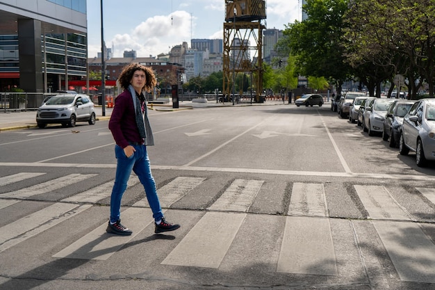 A portrait of a young Latin man with curly hair crossing the street on the pedestrian path.