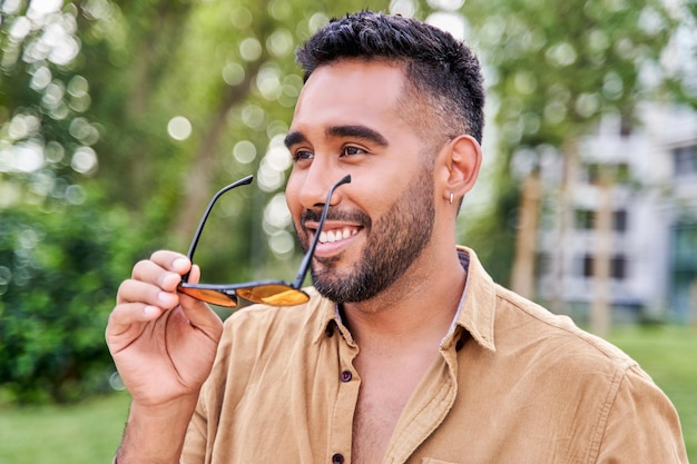 Portrait of a young latin man with sunglasses in hand and beard smiling