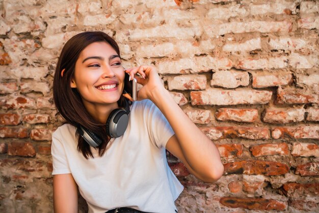 Portrait of young latin woman talking on the phone outdoors against brick wall. Urban and communication concept.