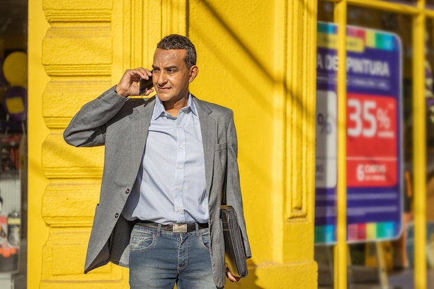 Portrait of a young latino man talking on the mobile phone over a yellow wall with copy space