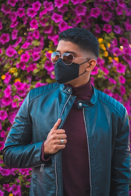 Portrait of a young Latino with pink flowers in the background. Jeans, leather jacket and brown shoes