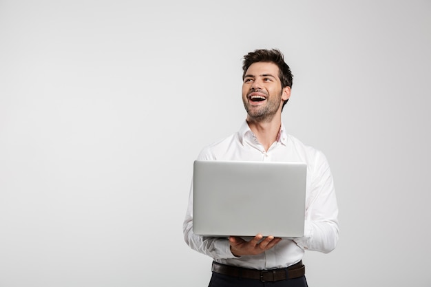 Portrait of young laughing businessman holding and using laptop isolated on white