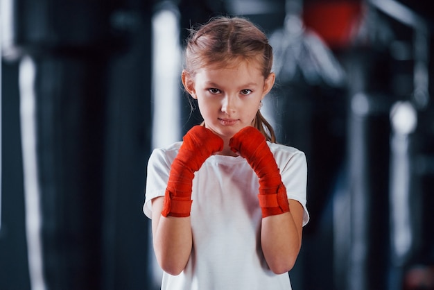 Портрет молодой маленькой девочки в спортивной одежде, которая находится в тренажерном зале, имеет день упражнений. Концепция бокса.