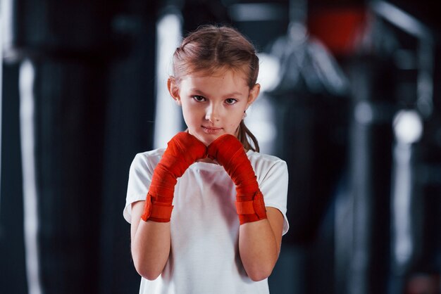 Photo portrait of young little girl in sportive wear that is in the gym have exercise day. conception of boxing.