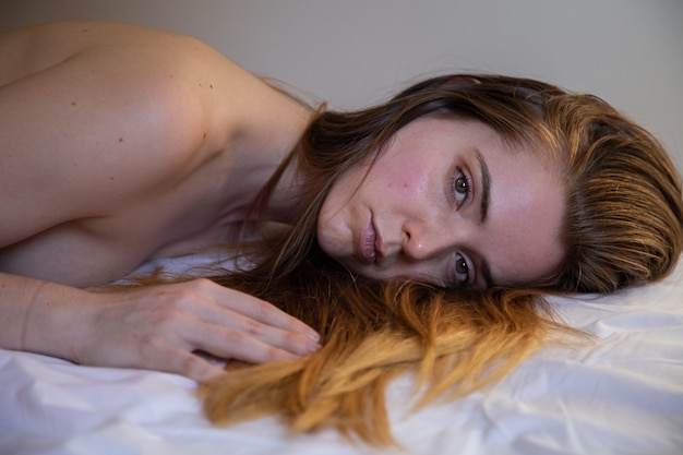Portrait of young lonely pretty woman with brown hair lying on bed and looking