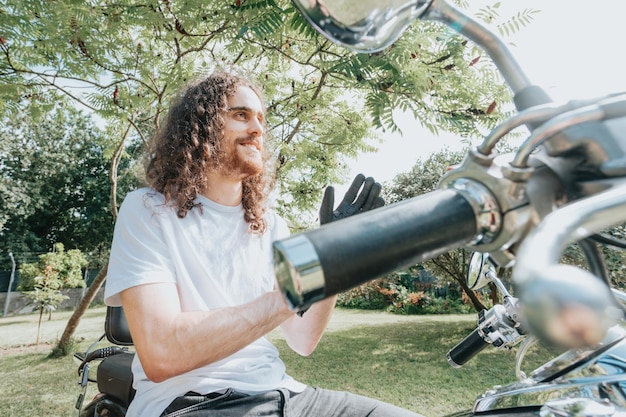 Portrait of a young long hair man in a motorbike using gloves doing a road trip. Travel concept. Gloves and rude hands holding a map over a old school motorbike.