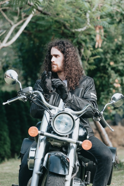 Portrait of a young long hair man, an old biker in a leather jacket on a retro bike, vintage classic motorcycle. concept of freedom and style, a hobby for life. copy space