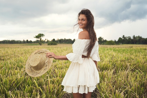 Portrait of young lovely woman holding straw hat in the rice field