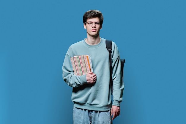 Photo portrait of young male college student in glasses with backpack on blue background