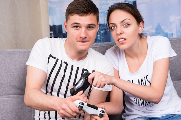 Portrait of young male and female gamers playing video game sitting on a couch together at home in a relaxed atmosphere