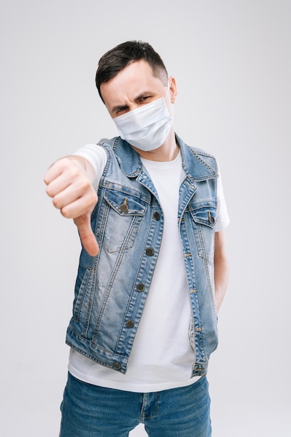 Portrait of young male wearing medical mask is showing thumbs-up gesture. Concept of wagering bright emotions by a professional actor.