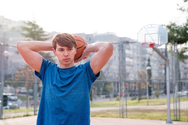 Portrait of a young man on a basketball court holding a basketball behind his head