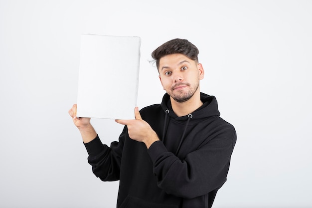 Portrait of young man in black hoodie holding empty canvas