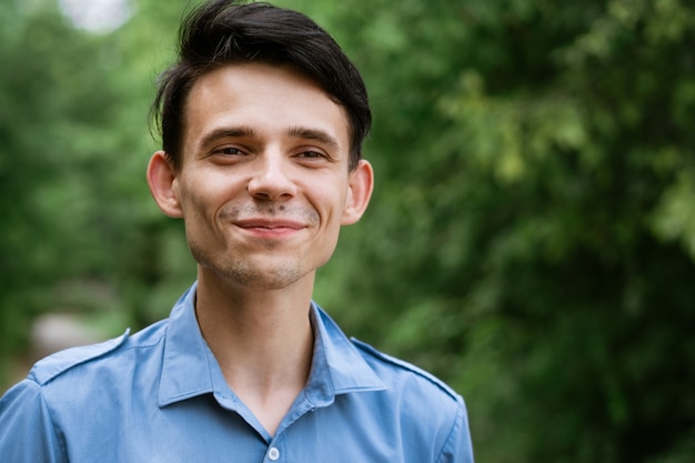 Portrait of a young man in a blue shirt on a green natural smiling