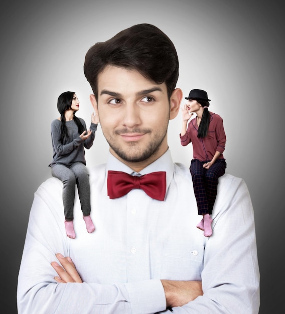 Photo portrait of a young man in a bow tie with two talking women sitting on his shoulders