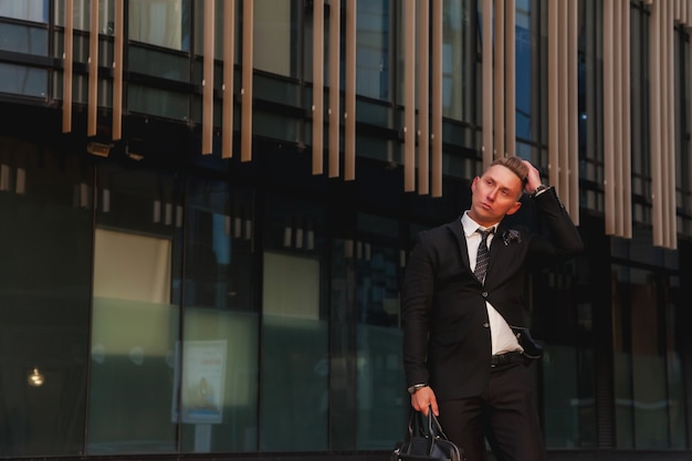 Portrait young man businessman with briefcase background business building corporate company, looking away, lifestyle. Male banker standing out from office located in financial district. Copy space