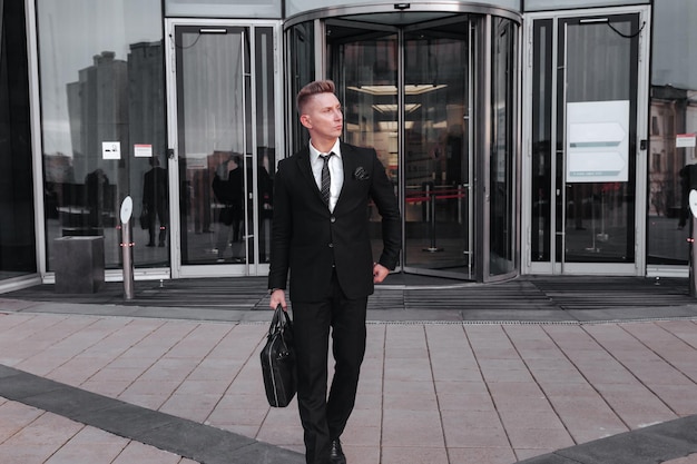 Portrait young man businessman with briefcase background business building corporate company, looking away, lifestyle. Male banker standing out from office located in financial district. Copy space