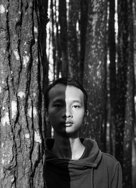 Foto ritratto di un giovane uomo vicino al tronco di un albero nella foresta