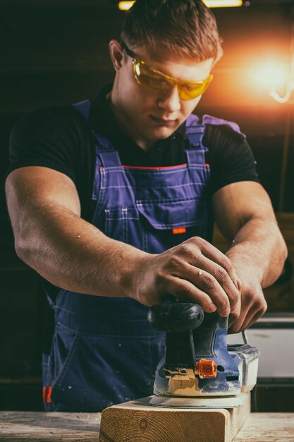 Portrait of a young man carpenter using electric sanding machine to polish a wood barin workshop