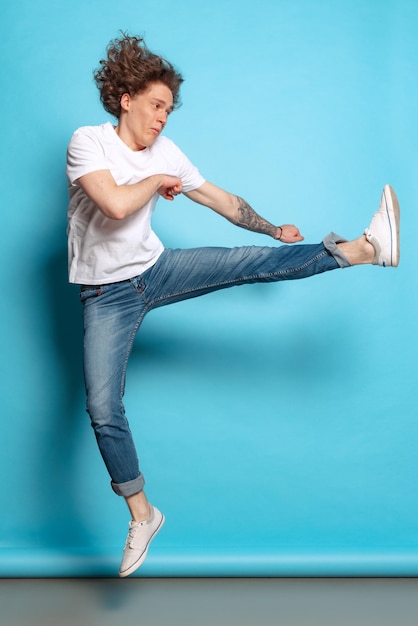 Portrait of young man in casual cloth cheerfully jumping\
isolated over blue studio background