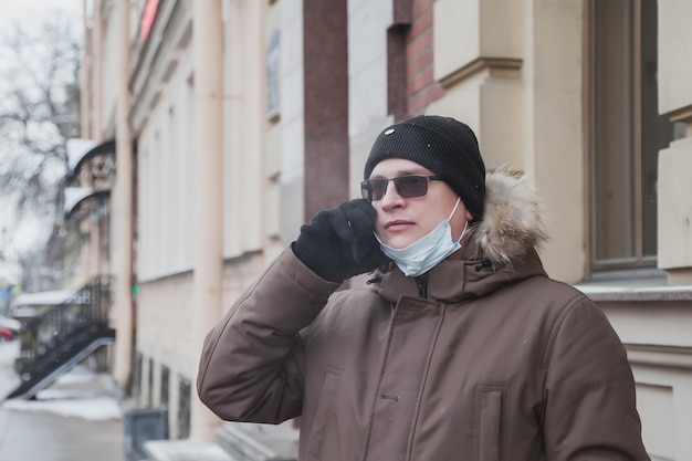 Portrait of young man in casual winter clothes with glasses and medical mask on walk city