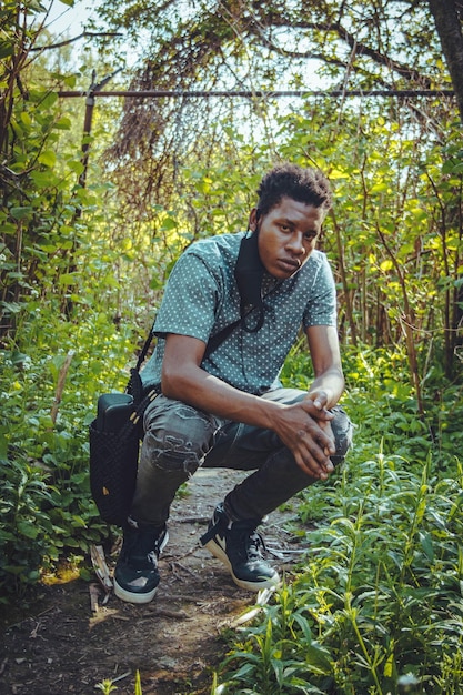 Photo portrait of young man crouching amidst plants in forest