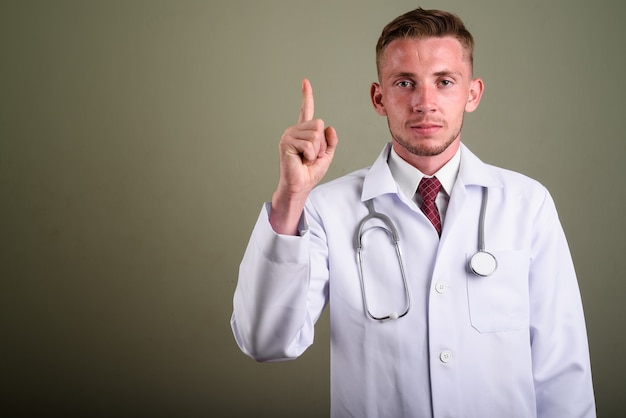 Portrait of young man doctor against colored wall