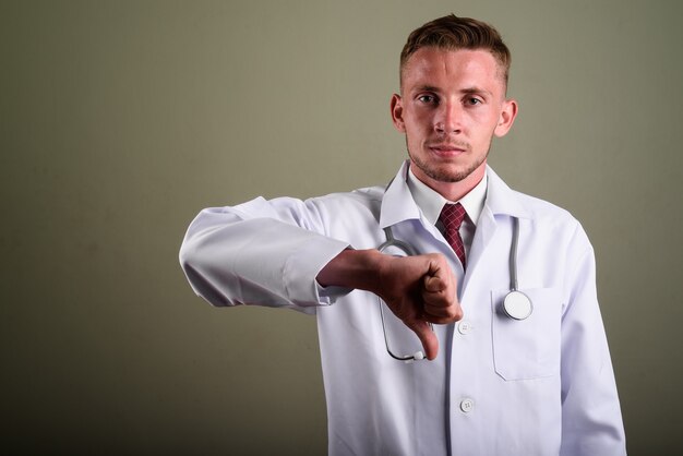 Portrait of young man doctor against colored wall