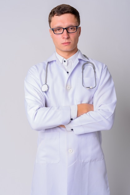 Portrait of young man doctor wearing eyeglasses against white wall