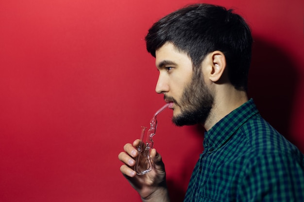 Foto ritratto di giovane uomo che fa trattamento di respirazione con inalatore mahold e olio essenziale isolato sulla superficie rossa