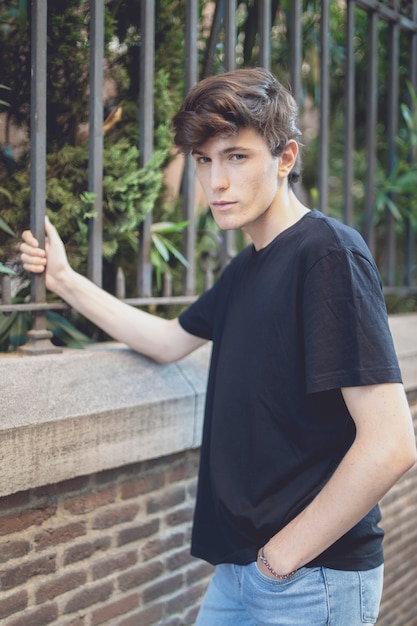 Portrait Young man dressed in black shed and jeans. Grabbed to an iron bar of the fence.