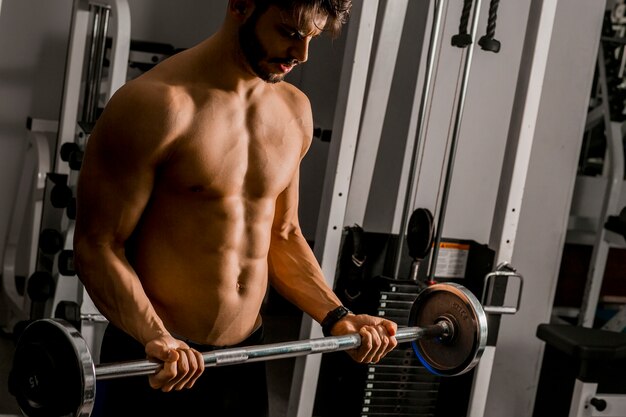 Portrait of young man flexing muscles with barbell in gym