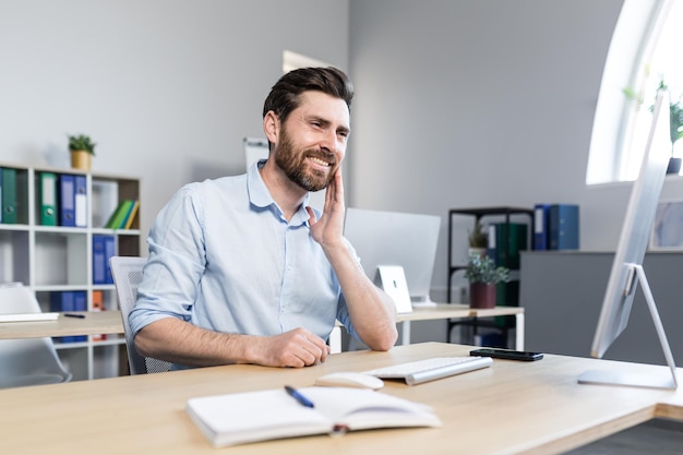 Ritratto di un giovane programmatore freelance che tiene la sua guancia mal di denti seduto a una scrivania in ufficio