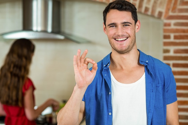 Portrait of young man gesturing in kitchen while woman cooking on stove 