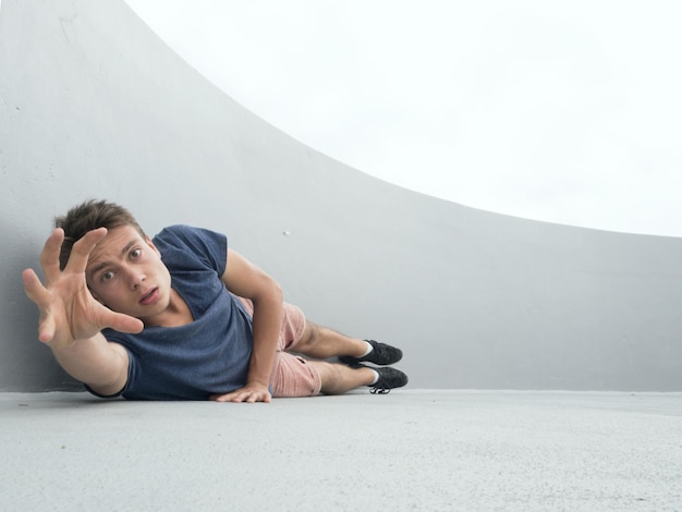 Photo portrait of young man gesturing while lying by wall on footpath