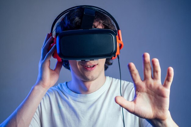 Portrait of a young man in the glasses of virtual reality on a gray wall background The concept of games in the mask of virtual reality
