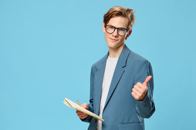 Portrait of young man holding book while standing against blue background