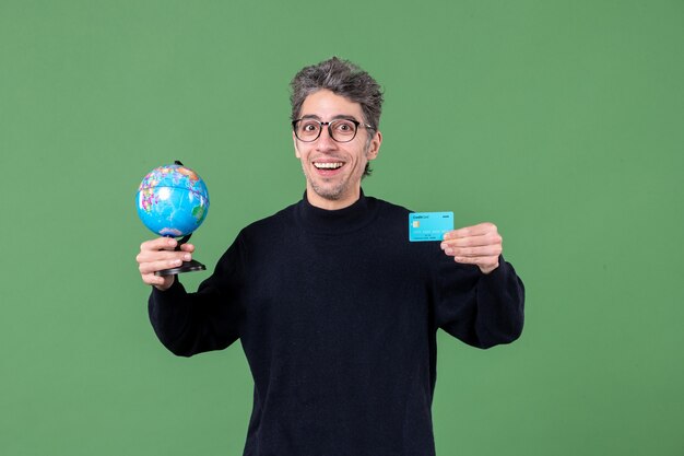 portrait of young man holding earth globe and credit card green background money nature male bank