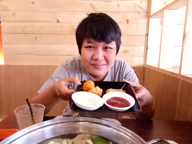 Portrait of young man holding food plate while sitting on chair at restaurant