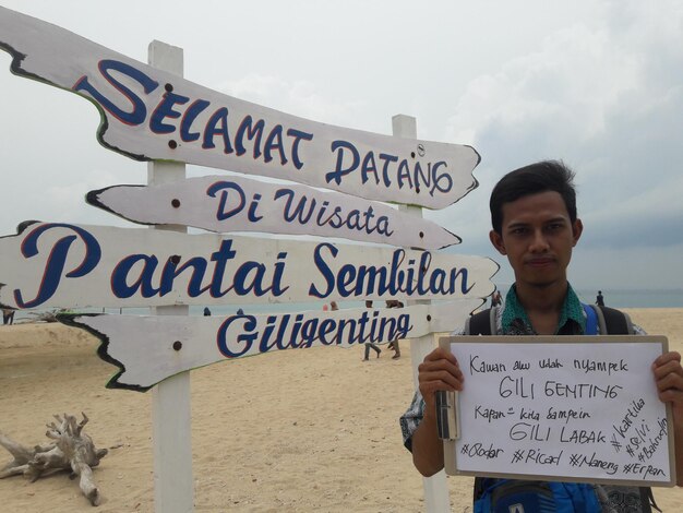 Photo portrait of young man holding paper with text while standing by information sign