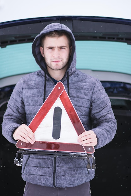 Foto ritratto di un giovane con un cartello in mano mentre si trova contro un'auto durante l'inverno