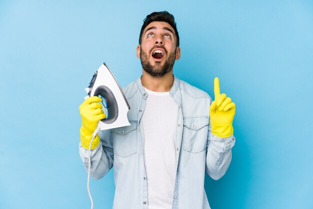 Portrait of young man ironing pointing upside with open mouth.