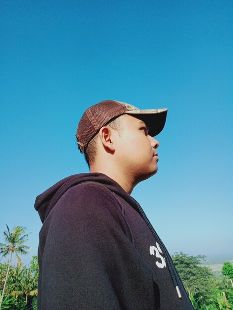 Portrait of young man looking away against blue sky