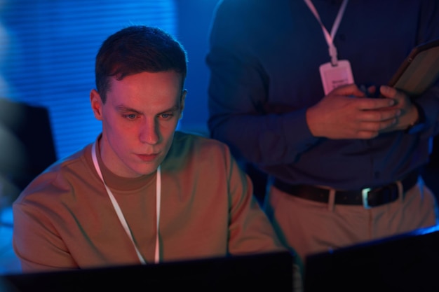 Portrait of young man looking at computer screen while working in data security center with blue and