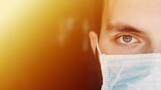 Portrait of a young man in a medical mask looks at the camera during the coronavirus pandemic