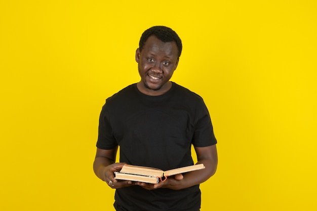 Portrait of a young man model holding books against yellow wall 