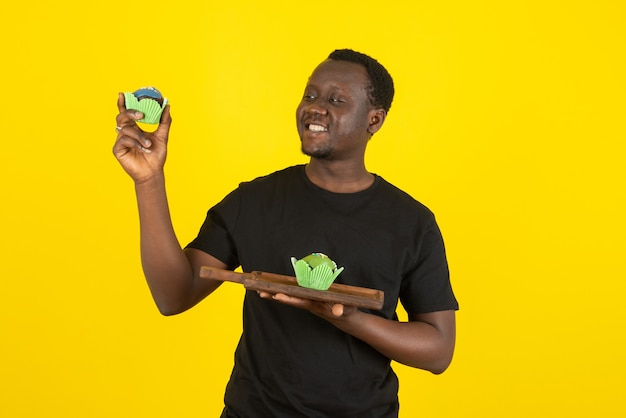 Photo portrait of a young man model holding delicious cupcakes against yellow wall