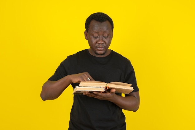 Portrait of a young man model reading a book against yellow wall 